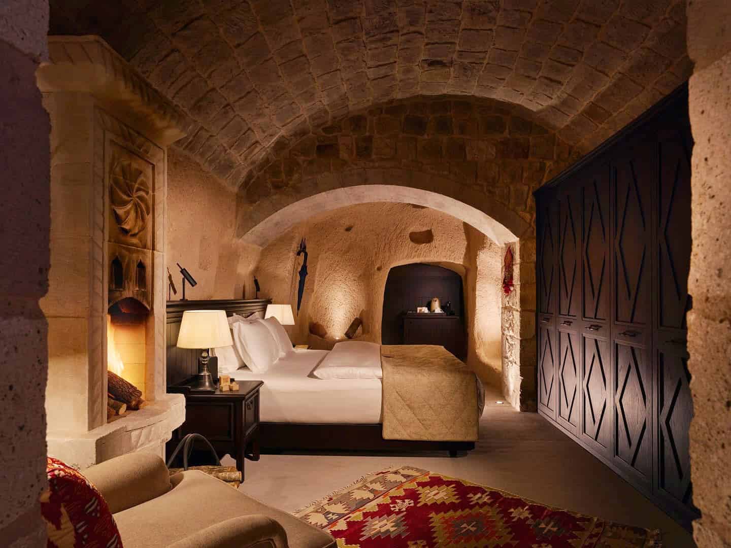 Dimly-lit cave hotel bedroom in Cappadocia, with a fireplacde