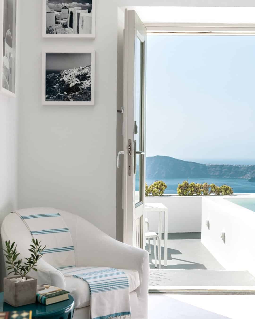 White chair inside a Grace Santorini room, by an open door with a view outside to the sea