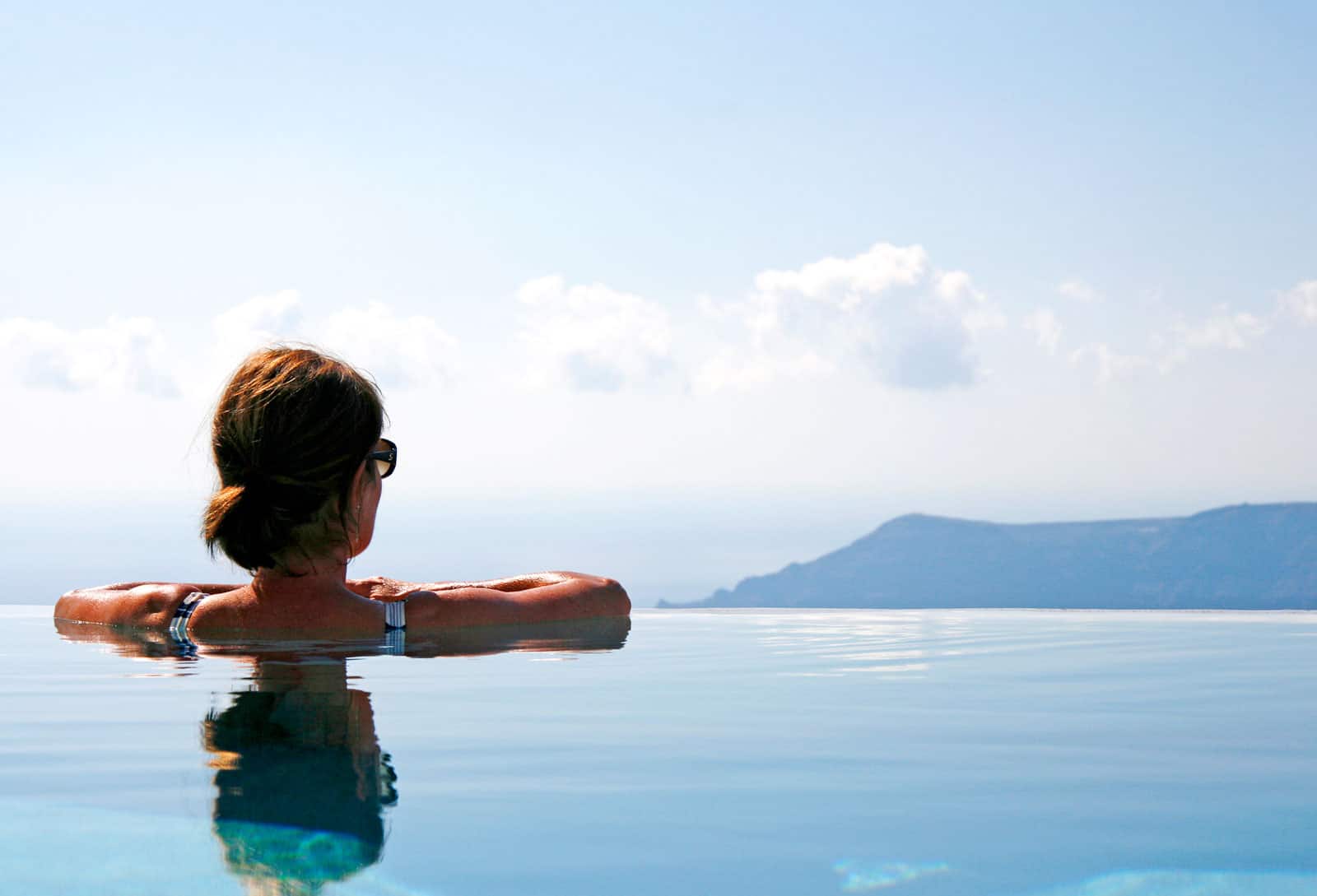 A woman standing in the Santorini Grace infinity pool, looking at the endless views