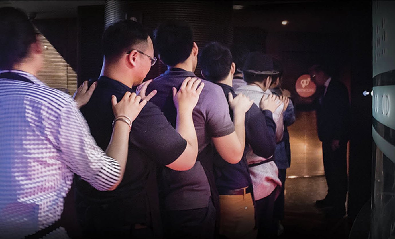 Group of men shuffle in a line in the dark to enter the dark dining restaurant in Bangkok.