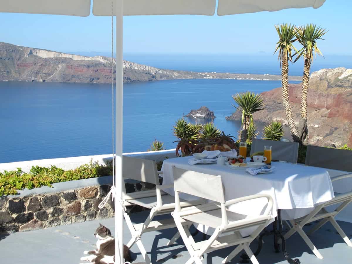 Table with white tablecloth set with breakfast, against a backdrop of turquoise sea