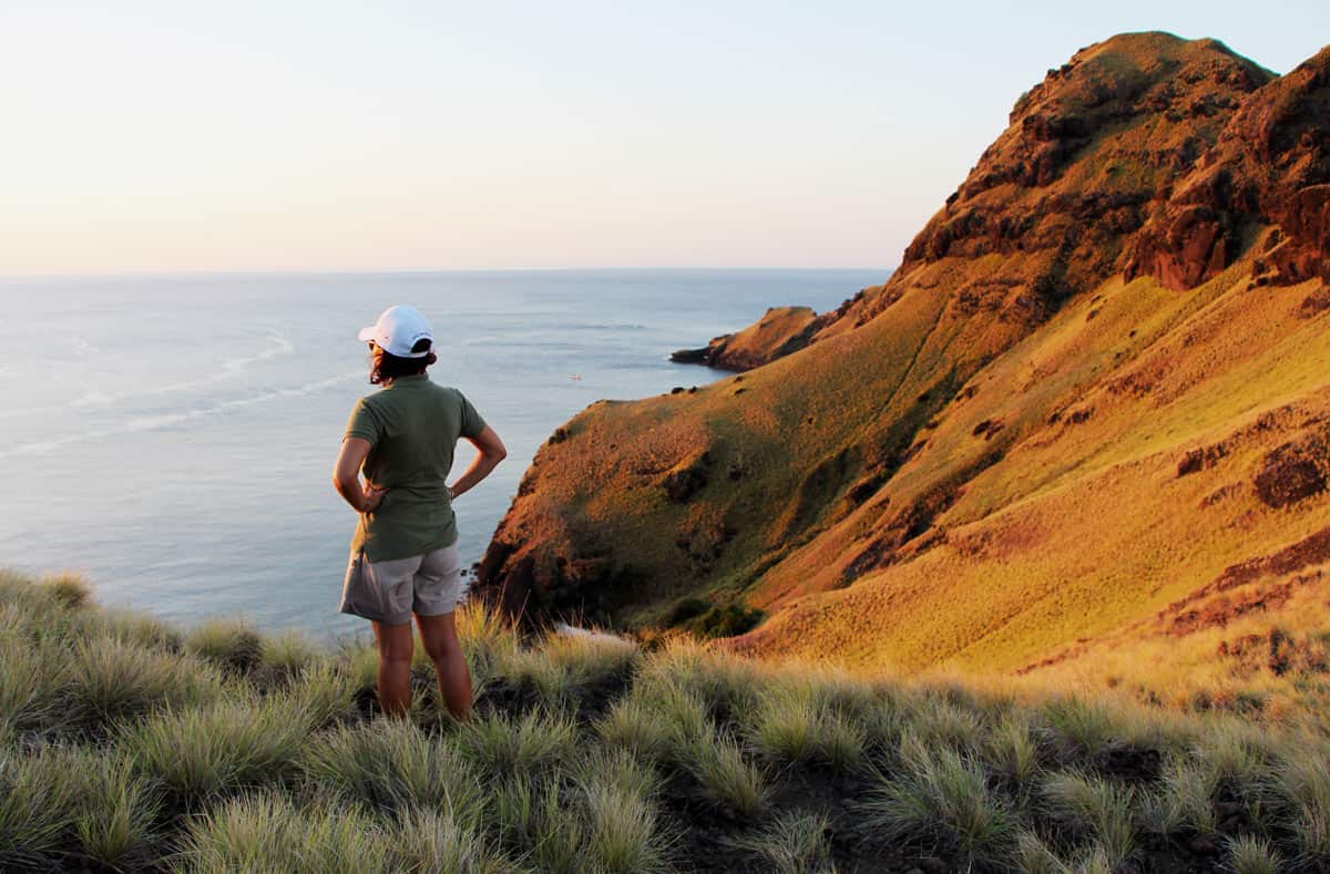 Woman looks out at sea with golden hills behind her