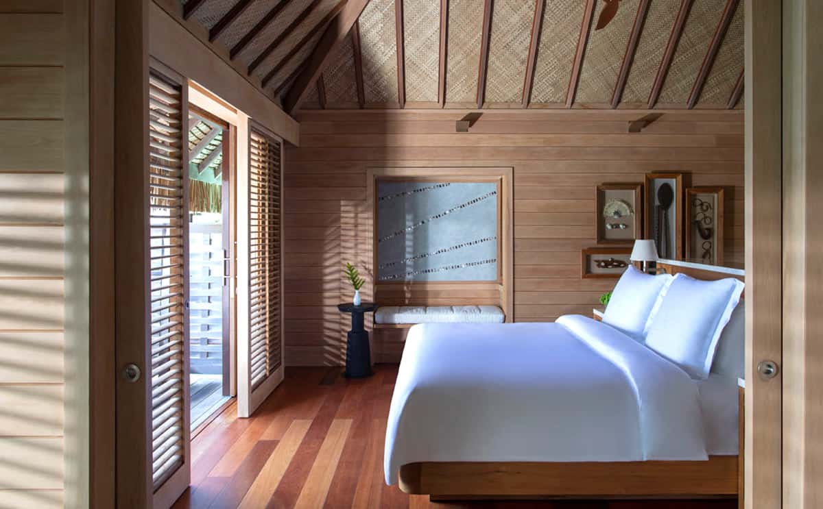 Overwater bungalow bedroom with wood floors and a king bed covered with a white duvet 