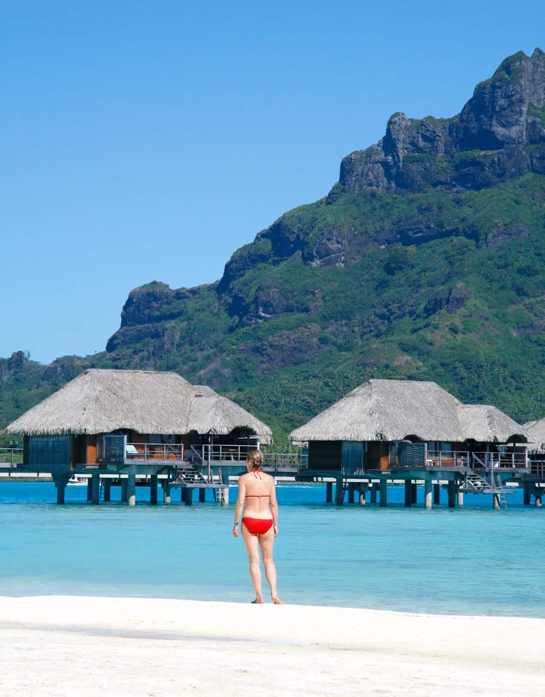 Woman in red bikini looking at overwater bungalows in Bora Bora