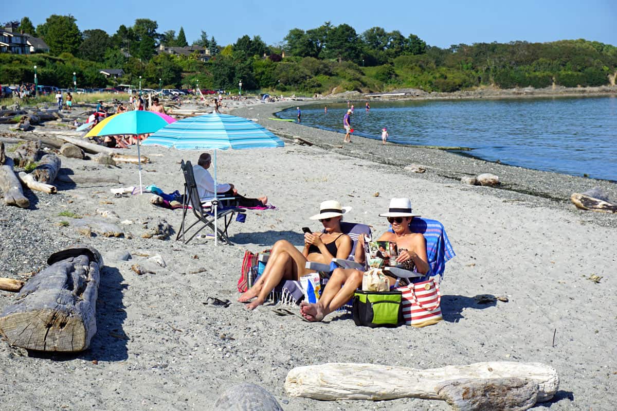 People in swimsuits sitting on the sand at Willows Beach, Victoria