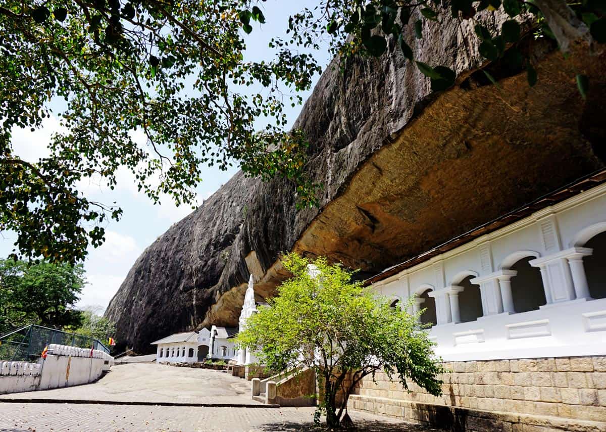 White building with arcaded façade and verandah, tucked beneath a huge rock overhang