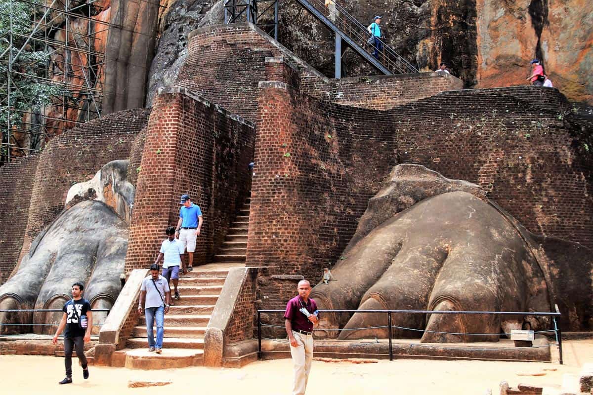 Visitors walk down steps between two giant stone lion paws at Sigiriya.