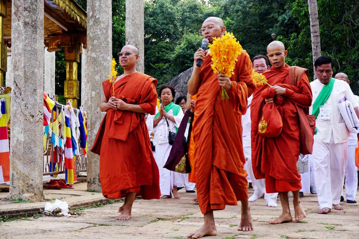 Buddhist monks in red robes lead worshippers in prayer at sacred Mihintale
