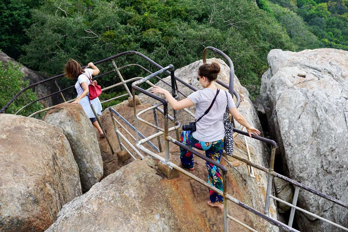 Two women make the barefoot descent back down boulders from the top of Mihintale.