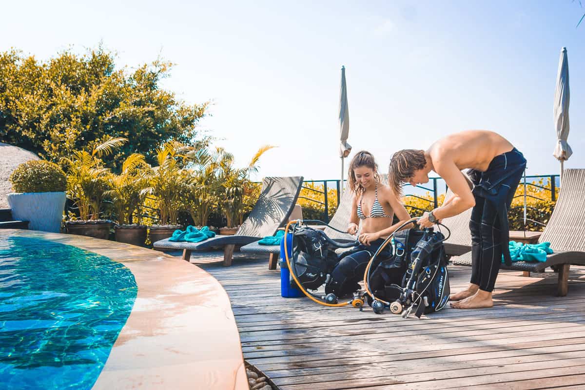 Couple putting on dive gear by the pool at Jamahkiri Dive Resort