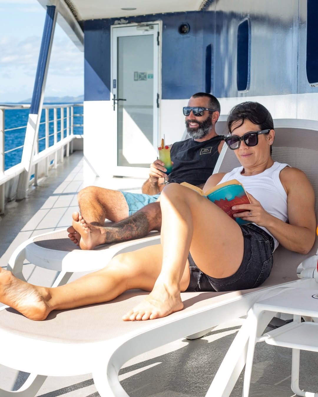 Couple in shorts and T-shirts reading on deck of Blue Lagoon Cruises