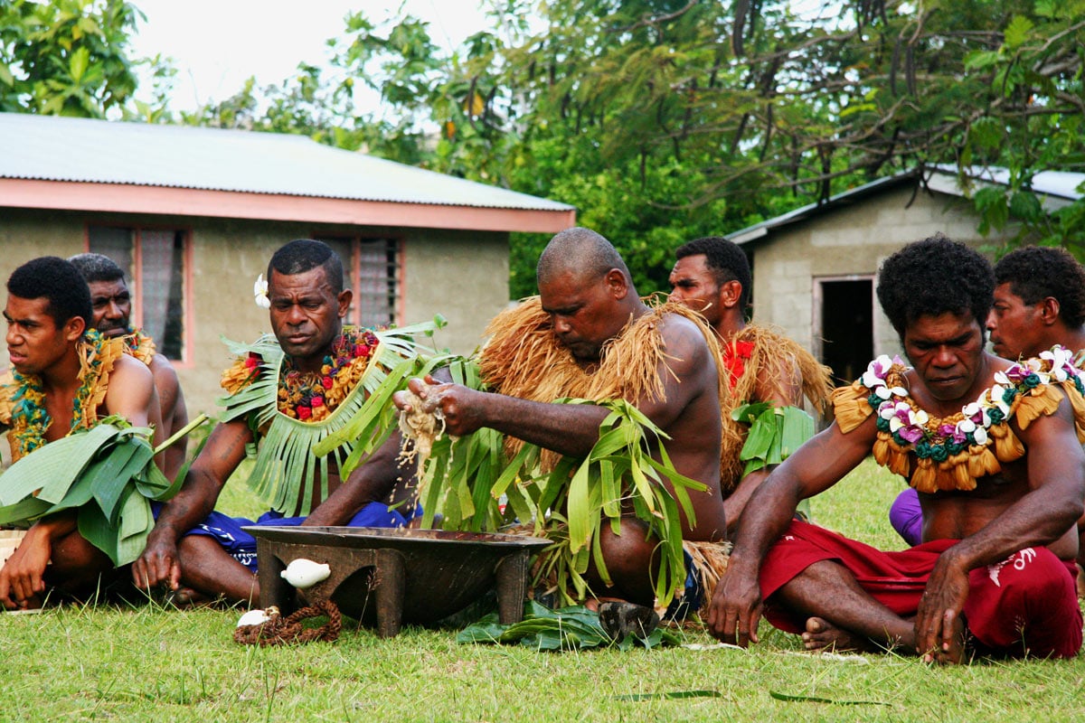 Fijian locals wearing skirts and grass necklaces make kava, the traditional Fijian welcome drink