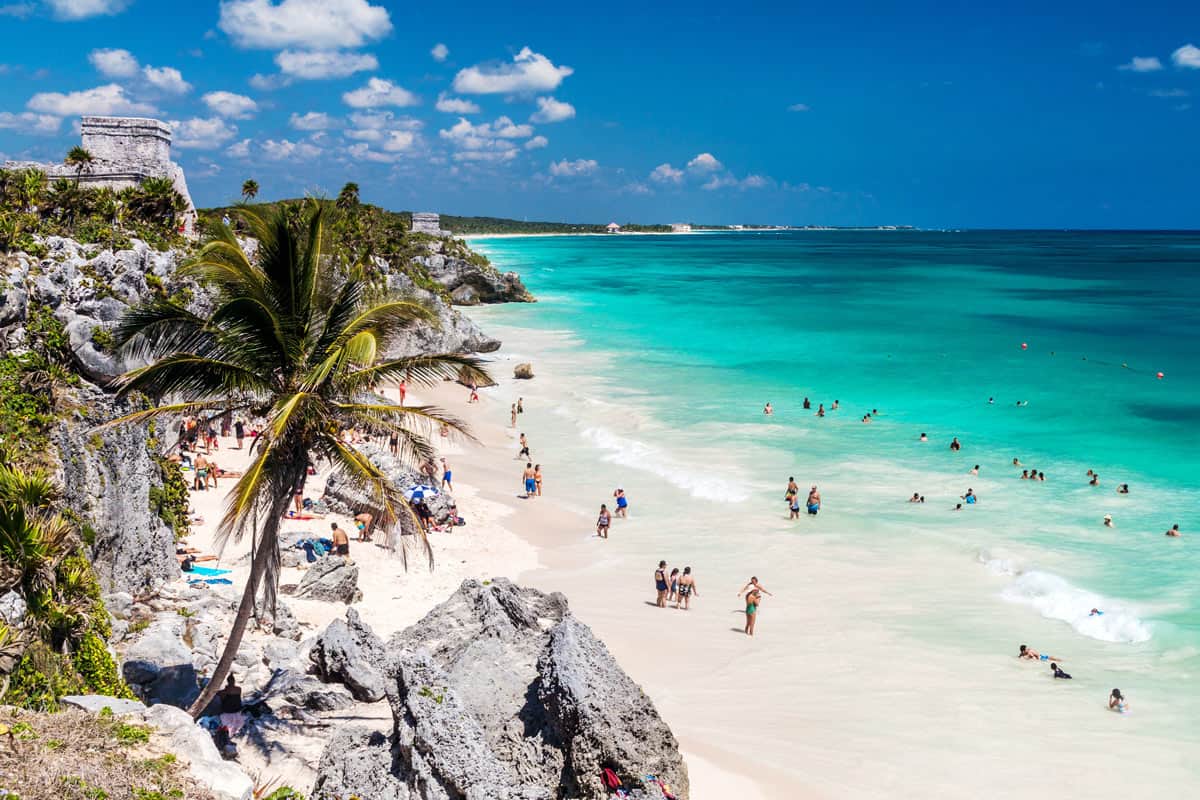 People swim at the white sand beach below the Tulum ruins