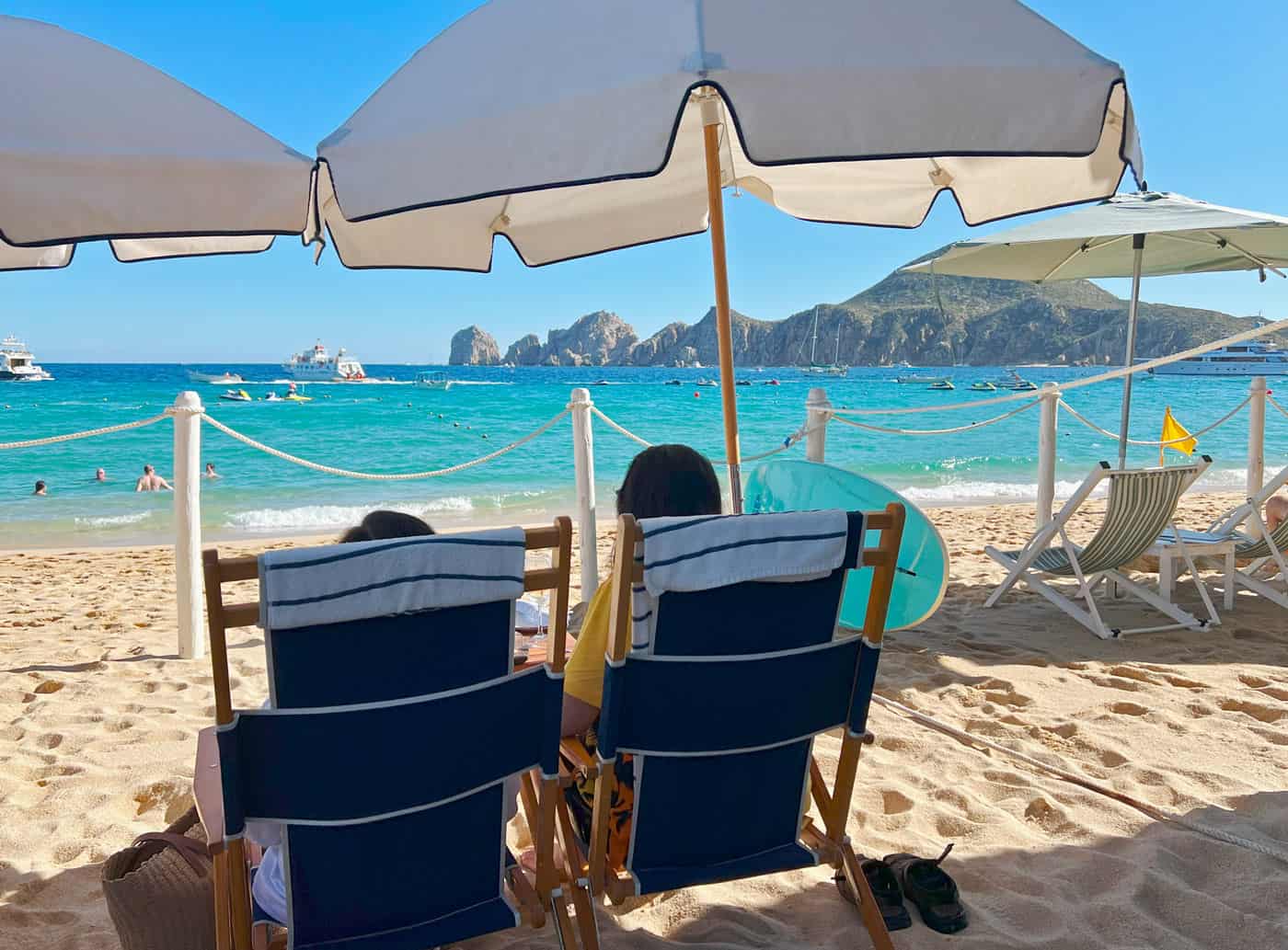 Couple in beach chairs on the golden sand Medano Beach, looking out over the turquoise sea at the rocky formations of Land's End