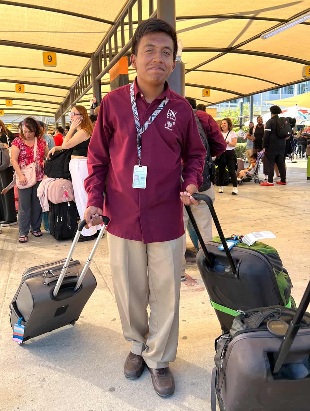 A greeter at the Los Cabos airport in a burgundy shirt with the logo "Epic" on it, pulling two suitcases