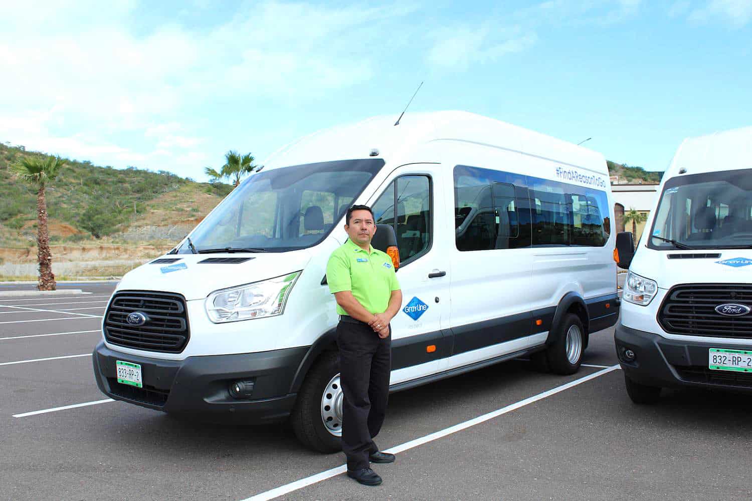 Gray Line Los Cabos driver in a lime green shirt stands outside his white van at the Cabo airport.