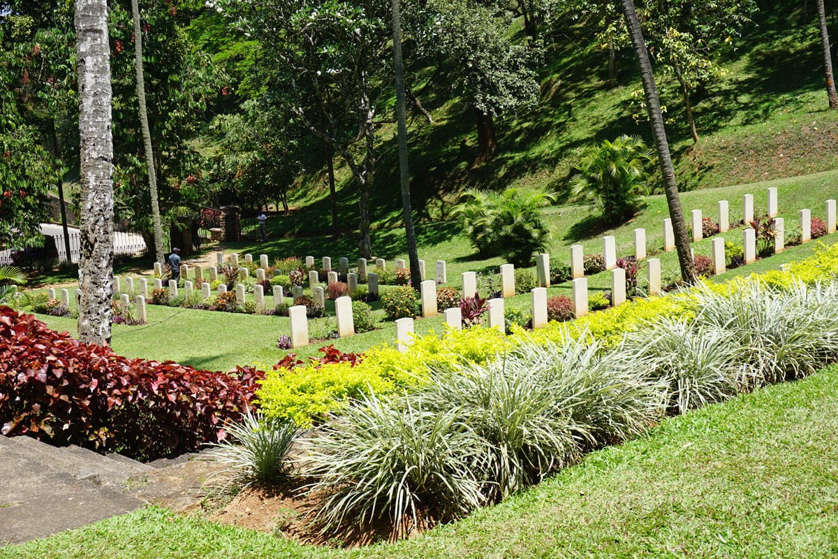 Rows of white gravestones among manicured lawns, tropical palms and colorful gardens at Kandy War Cemetery in Sri Lanka