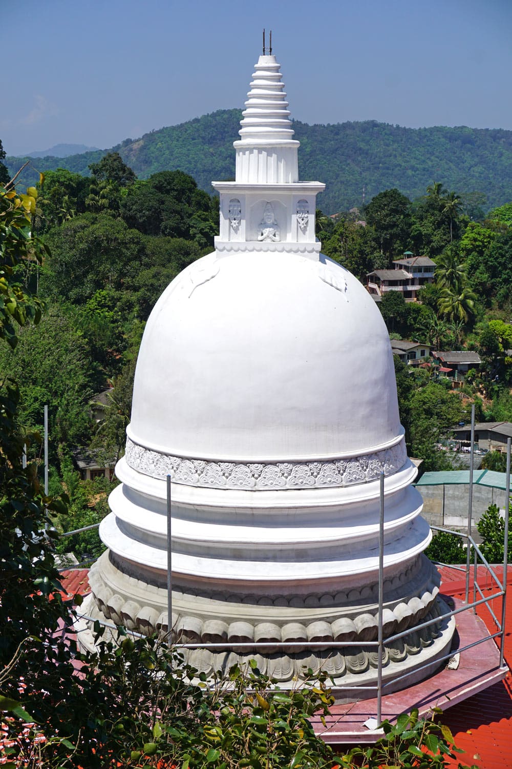 Gleaming white stupa against a green backdrop of trees