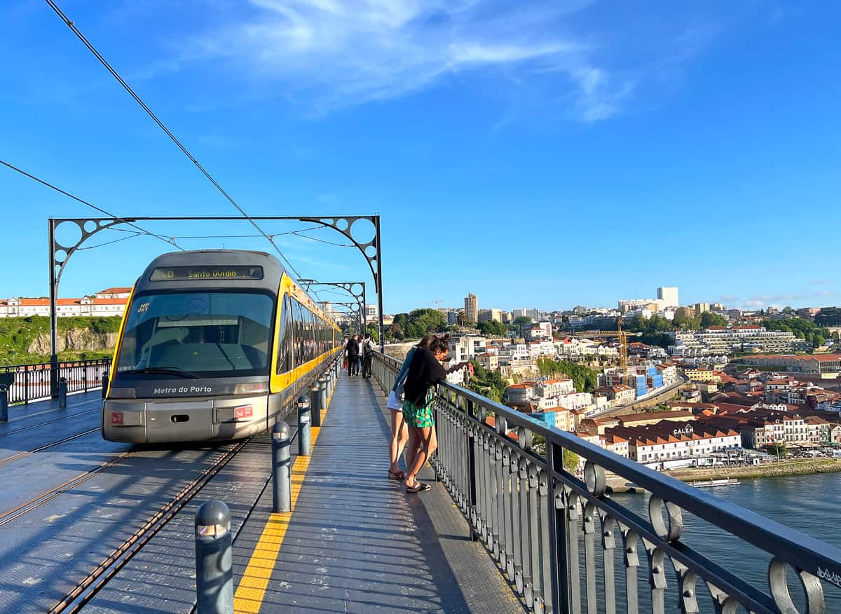 A yellow tram passes pedestrians on the Dom Luis 1 Bridge in Porto.