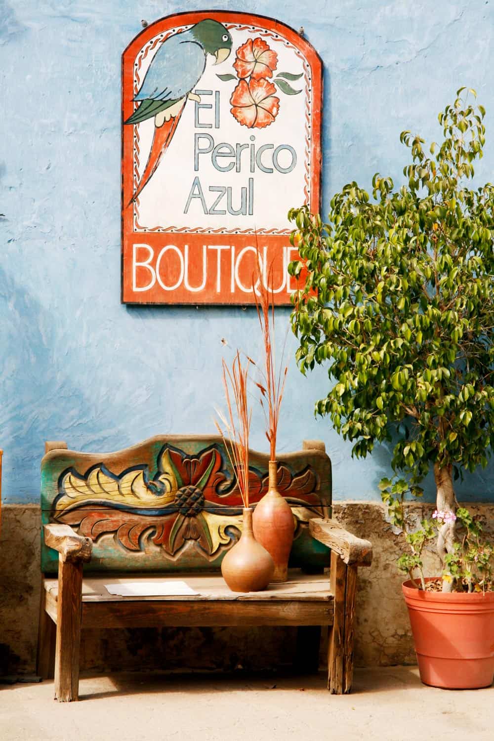 Colorful El Perico Azul boutique sign above a carved wooden bench against a blue wall in Todos Santos, Mexico