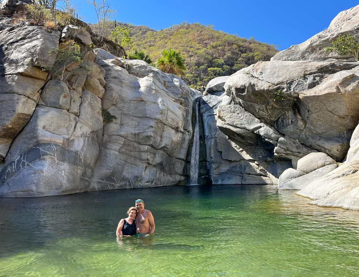A couple stands in a crystal-clear natural pool beneath the Sol de Mayo waterfall, near Los Cabos, Mexico.