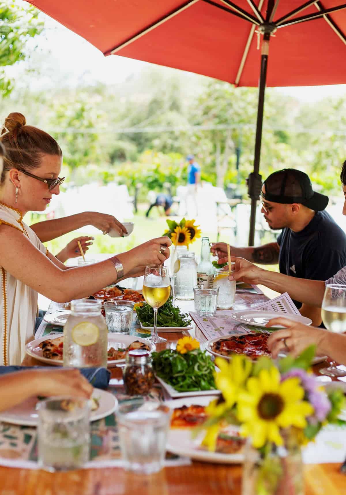 Friends enjoy a farm-to-table lunch of wood-fired pizzas, fresh salads and wine under a red umbrella at Flora Farms in Los Cabos.