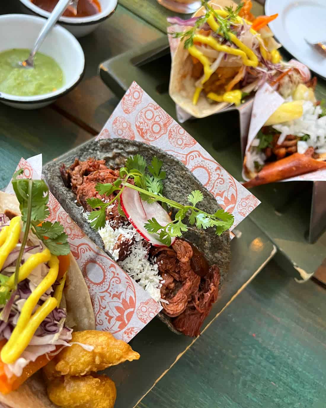 Colorful gourmet tacos at La Lupita in Cabo San Lucas, including crispy shrimp tacos and a shredded meat taco in a black tortilla with cilantro and radish
