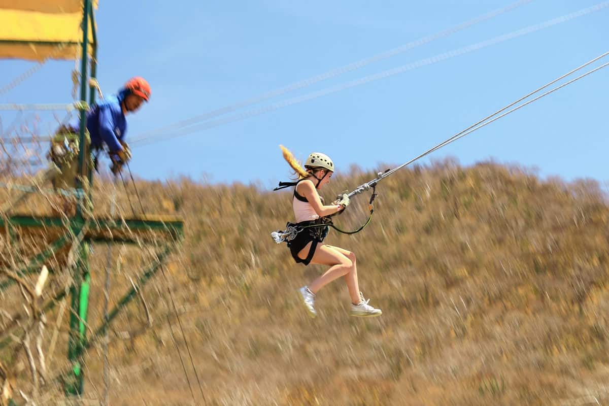 Woman in a helmet and harness launches from a zipline platform over the desert in Cabo.