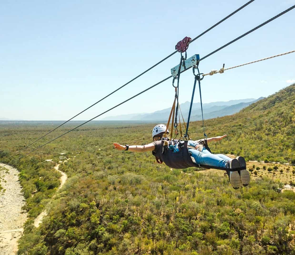 Person soars face-first on a Superman-style zipline high above the rugged desert landscape in Los Cabos.