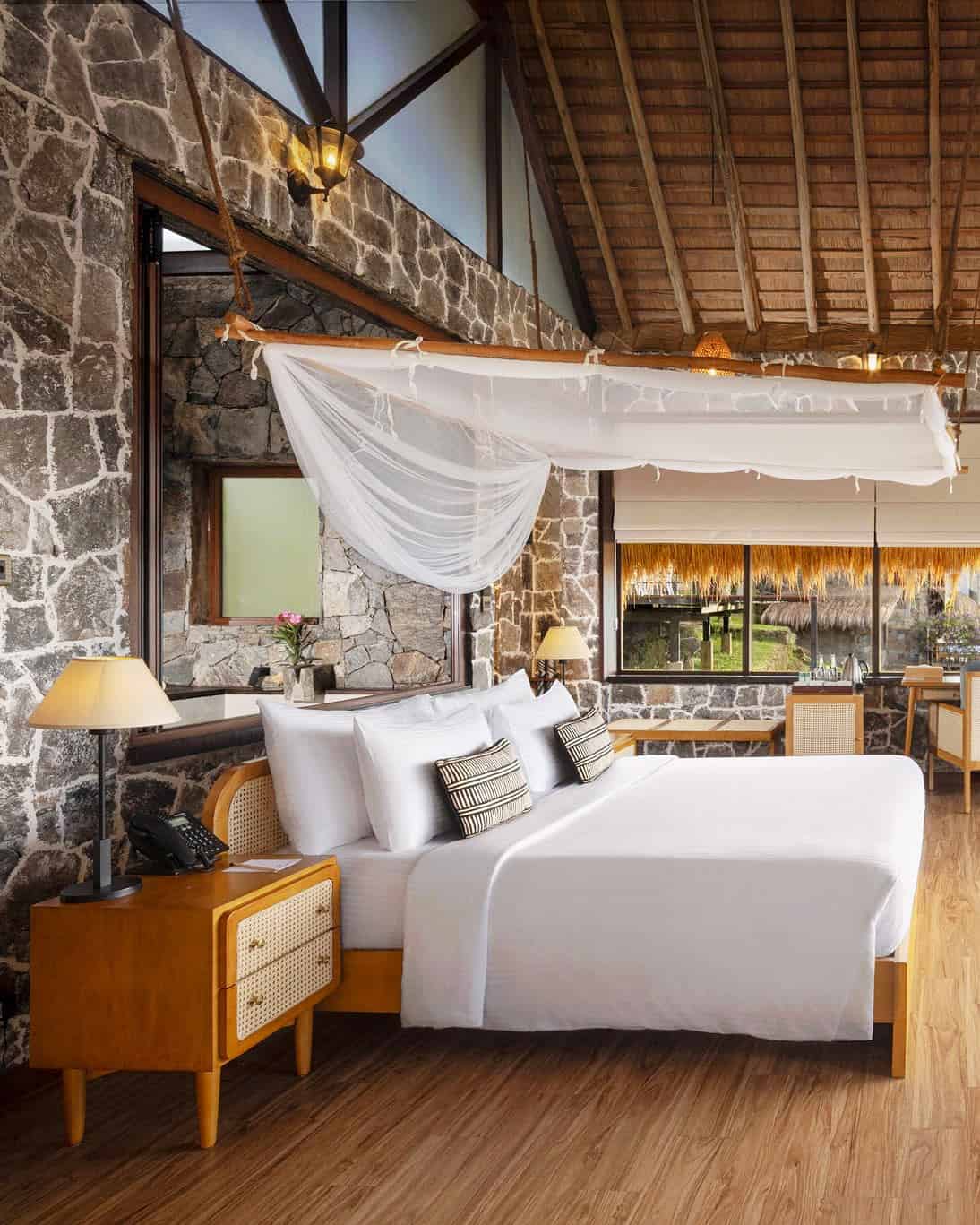 Guest room at 98 Acres Resort & Spa with a canopy bed, stone walls and thatched ceiling