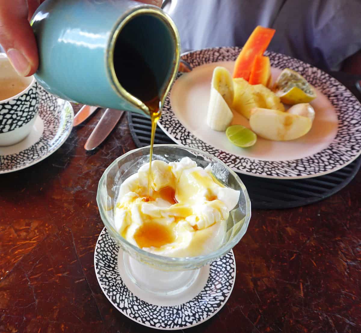 Pouring a small blue jar of treacle over a glass vase of buffalo curd