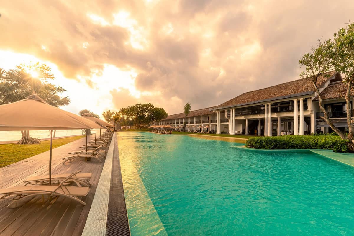 The turquoise infinity pool at The Fortress Resort & Spa glows beneath a golden-orange sunset sky.