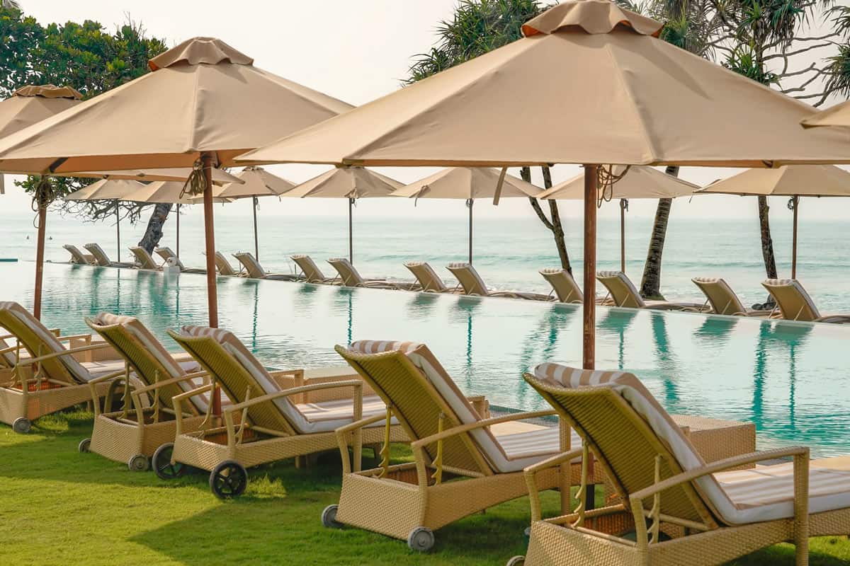 Turquoise pool overlooking the ocean, surrounded by lounge chairs shaded by beige umbrellas