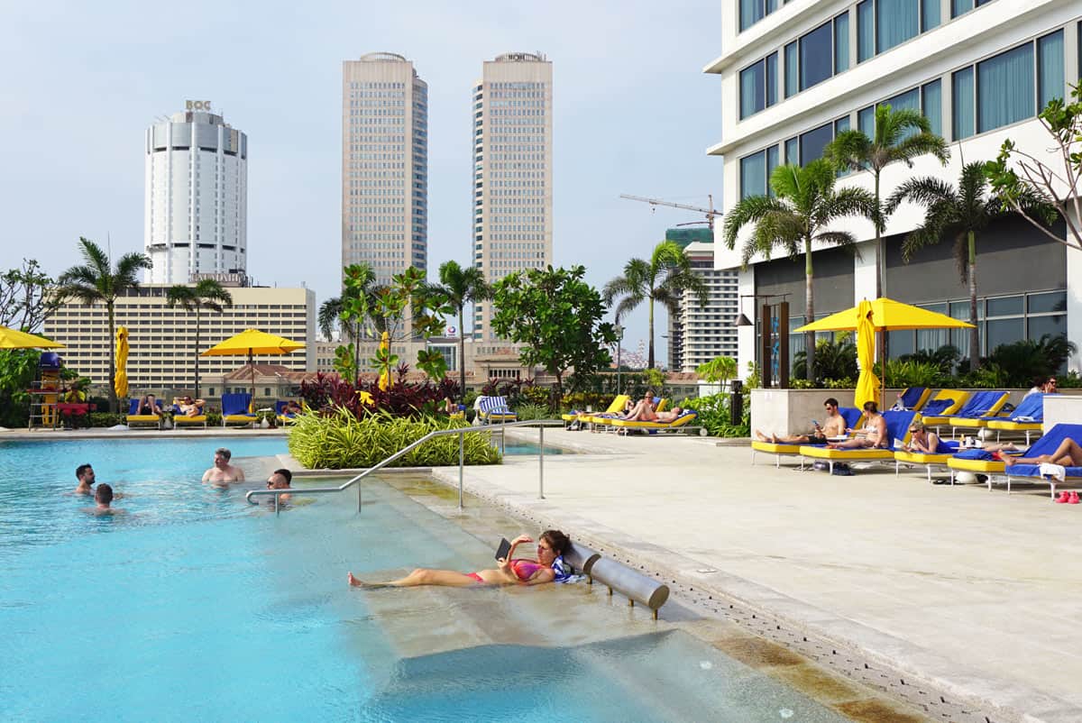 Guests relax in and around the  rooftop pool at Shangri-La Colombo, lined with yellow-cushioned loungers and umbrellas.
