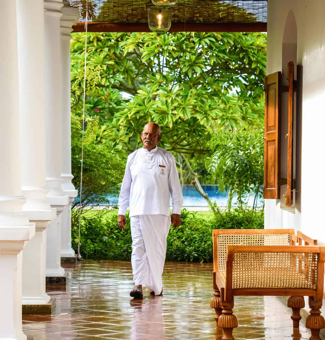 Staff member in white pants and shirt walks along the columned veranda of an historic hotel mansion in Sri Lanka.