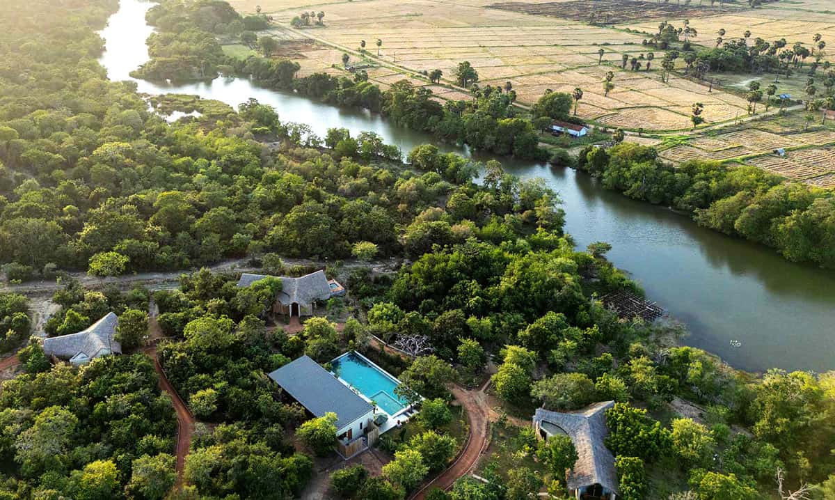 Aerial view of thatched-roof chalets in green jungl at Taru Villas Villu, beside the Kala Oya River, near Wilpattu National Park