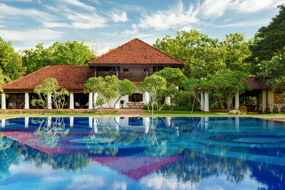 Large turquoise swimming pool in front of the historic, white-pillared mansion at Uga Ulagalla