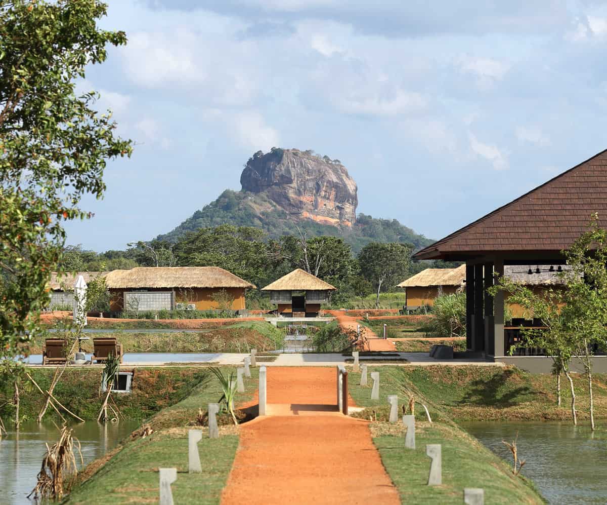 Orange sandy path to reception of Water Garden Sigiriya, with brown rock of Sigiriya looming behind