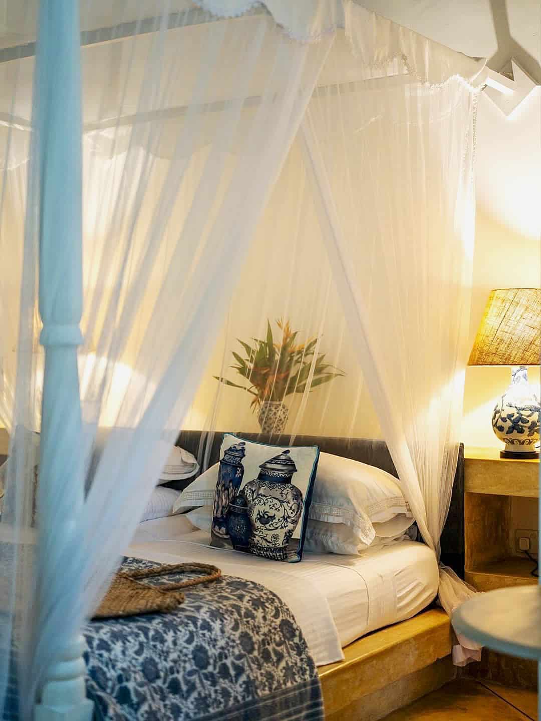 Four-poster bed with white gauzy linens and blue cushion