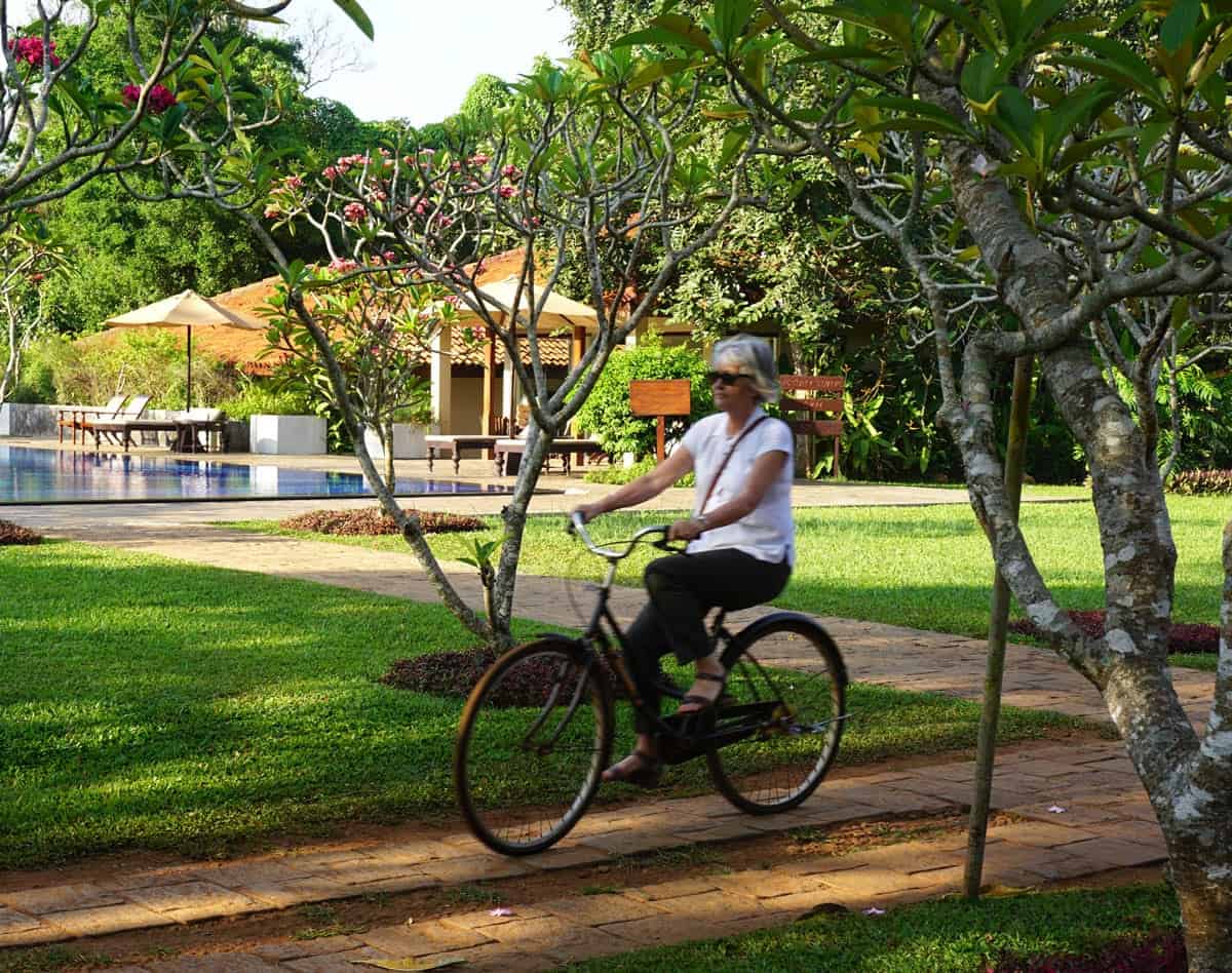 A woman rides a bicycle past the main pool, through tropical gardens at Uga Ulagalla.