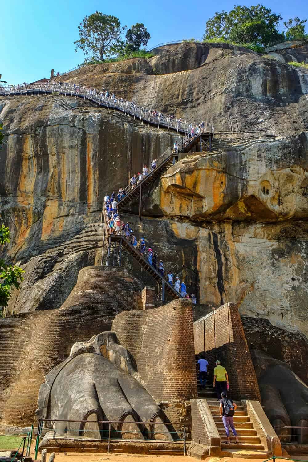 Steep stone and metal staircase carved into Sigiriya Rock, with dozens of visitors climbing up it