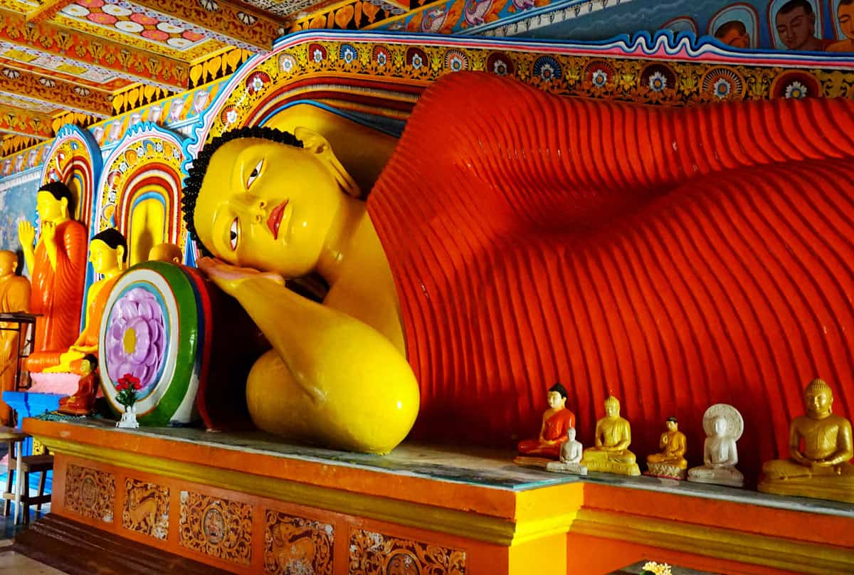 Large reclining Buddha in a red robe surrounded by smaller Buddha statues in Anuradhapura