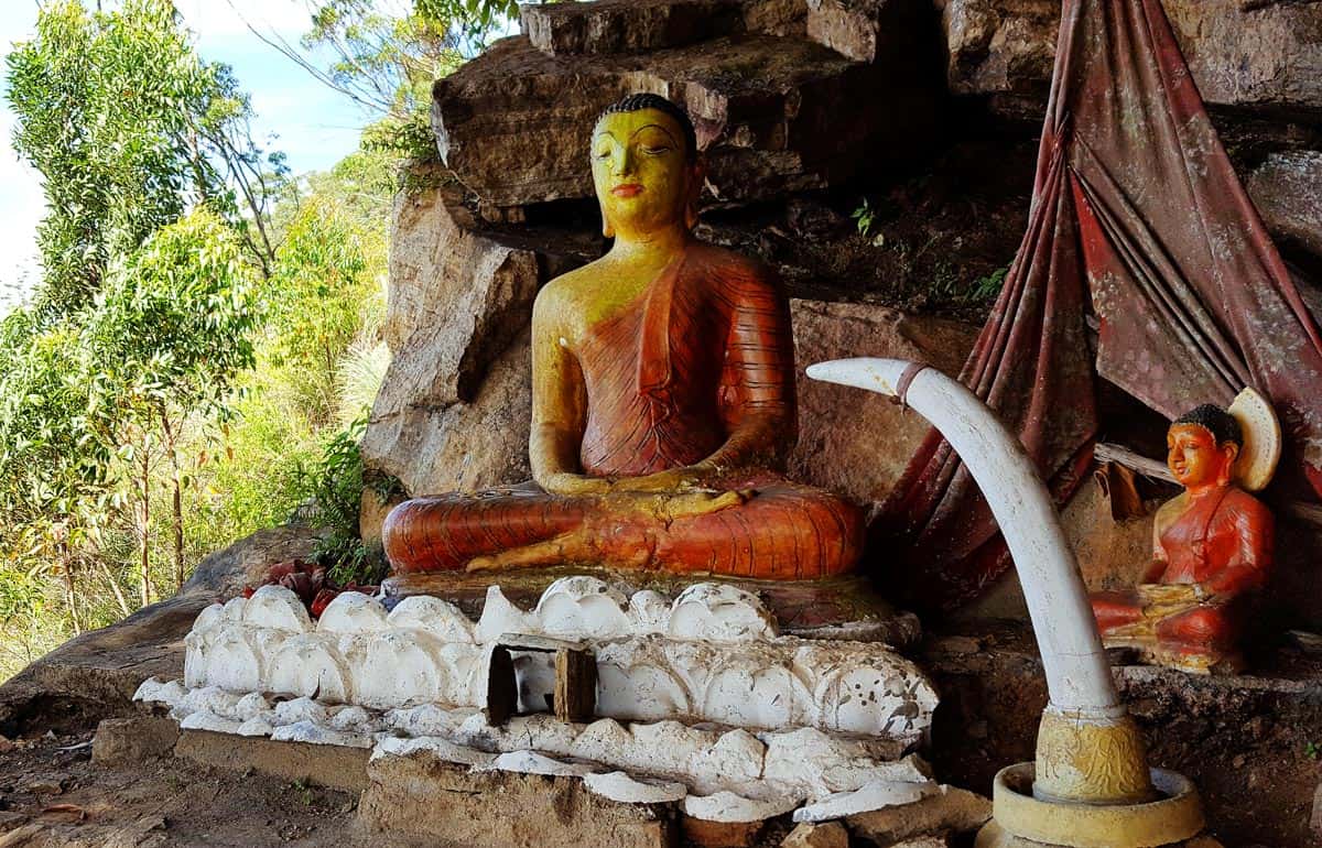 Seated Buddha statue in red robe inside a cave at the top of Ella Rock