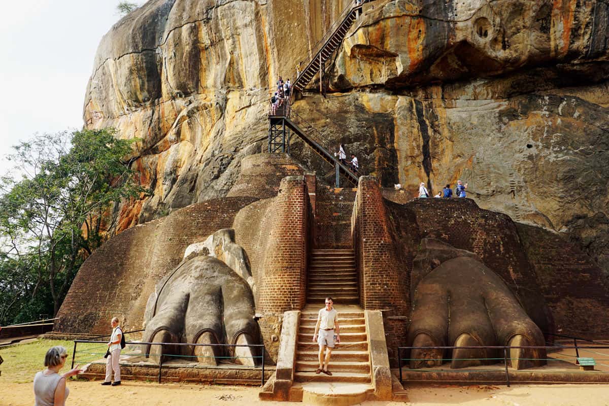 Two lion's paws carved into the golden-brown rock of Sigiriya, with a man walking between them