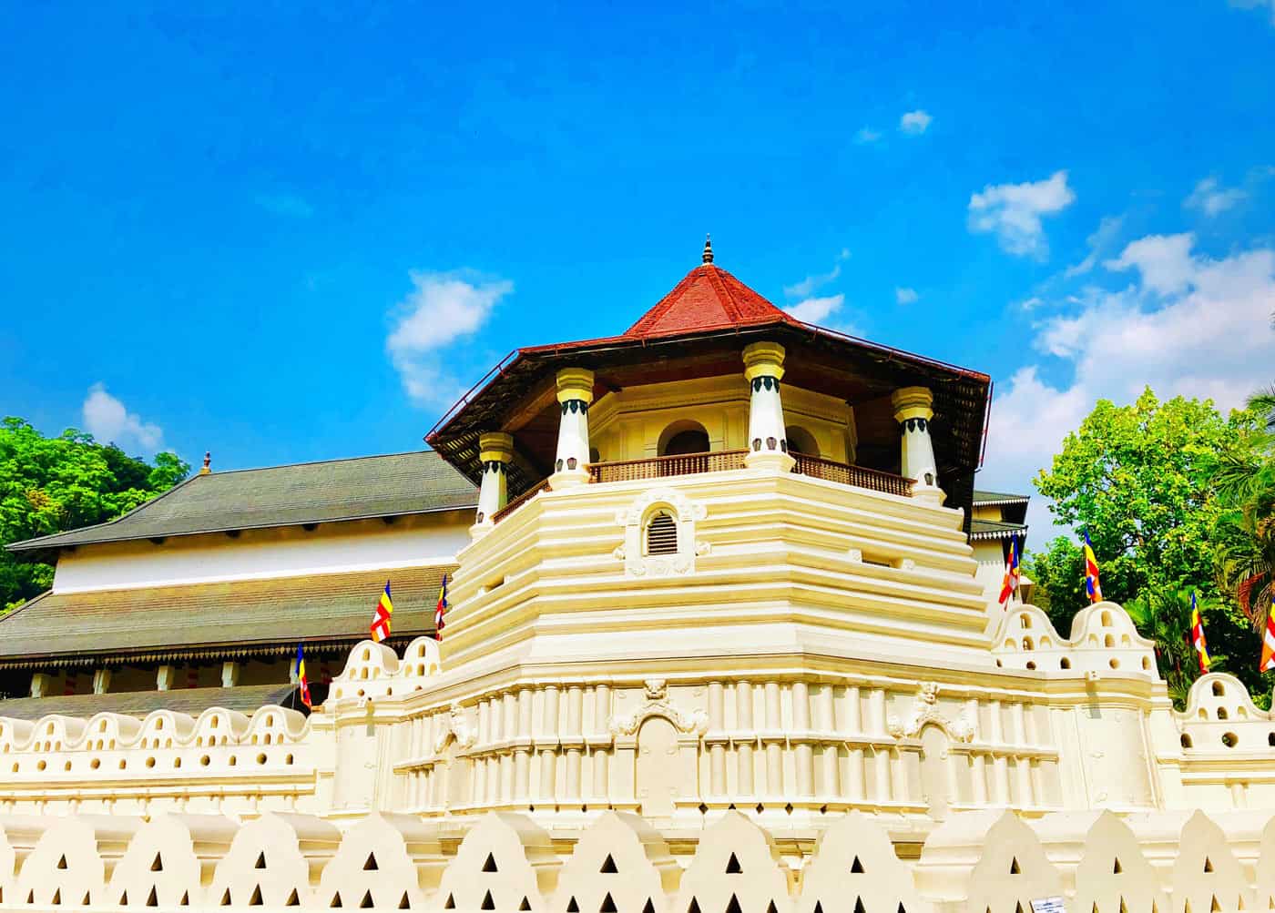 Temple of the Sacred Tooth Relic in Kandy, with white walls, red-tiled roof and Buddhist flags