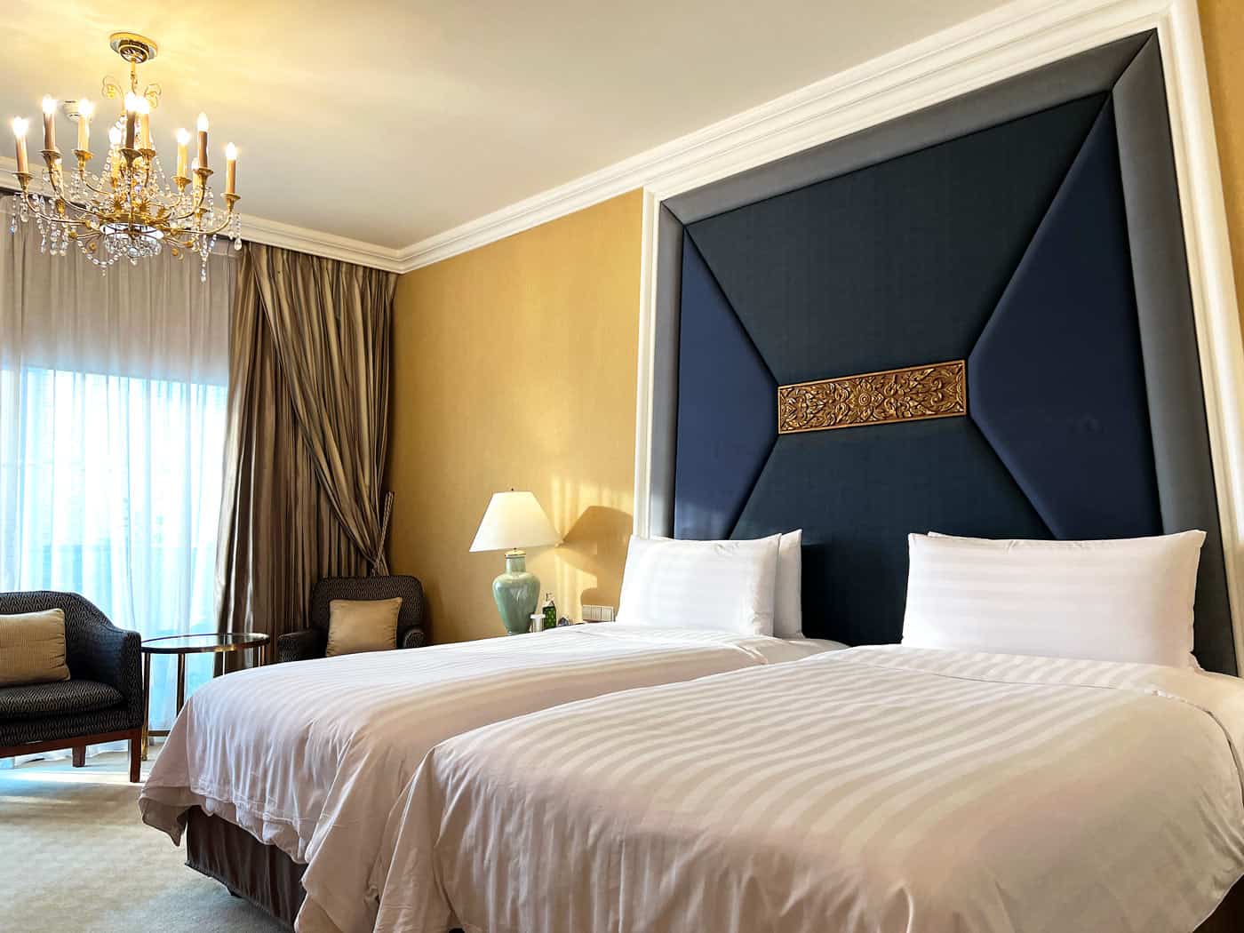 Krungthep Wing River View Room at Shangri-La Bangkok with twin beds, a dramatic blue headboard, chandelier and private balcony.
