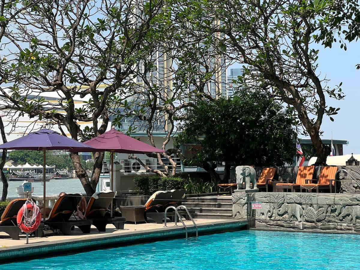 Krungthep Wing swimming pool at Shangri-La Bangkok, with orange-cushioned loungers, leafy trees and views of the Chao Phraya River