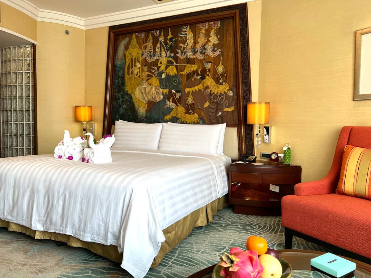 Shangri-La Bangkok Deluxe River View Room with a king bed, Thai-style painted headboard, red armchair and fresh tropical fruit
