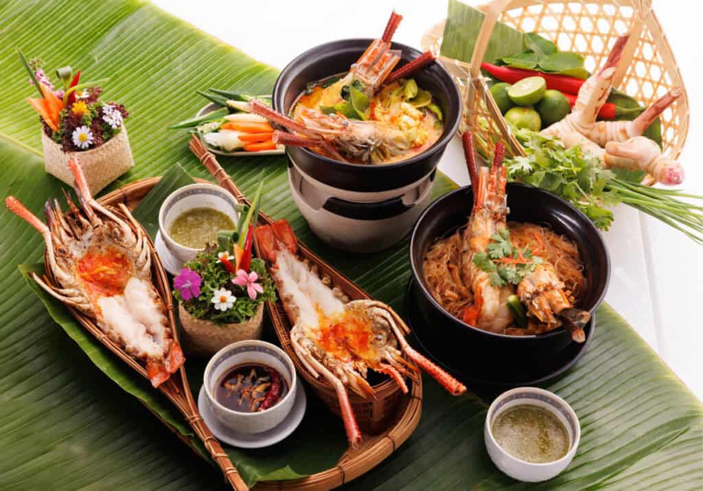 A spread of Thai seafood dishes at Salathip include grilled river prawns and prawn curry, served on banana leaves with dipping sauces.