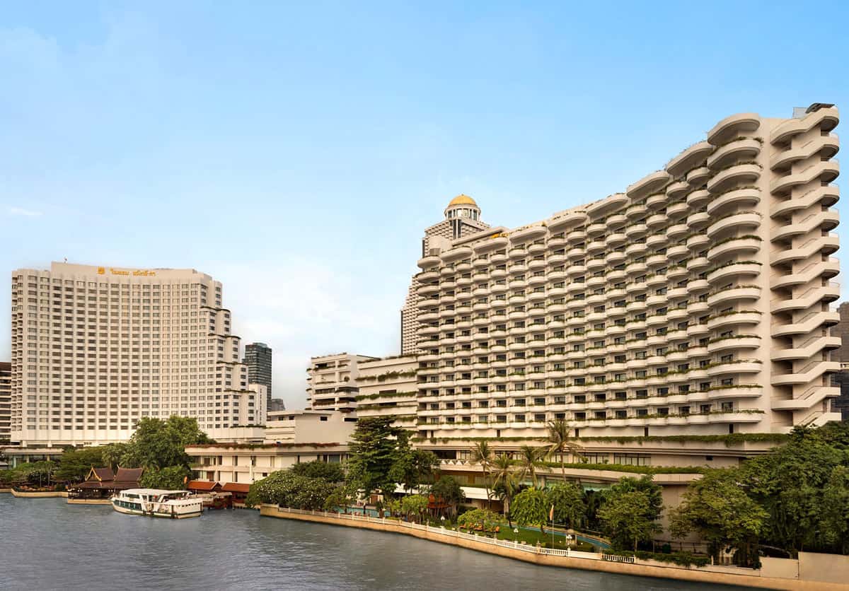 The two cream-colored towers of the Shangri-La Bangkok hotel rise above tropical gardens along the Chao Phraya River.